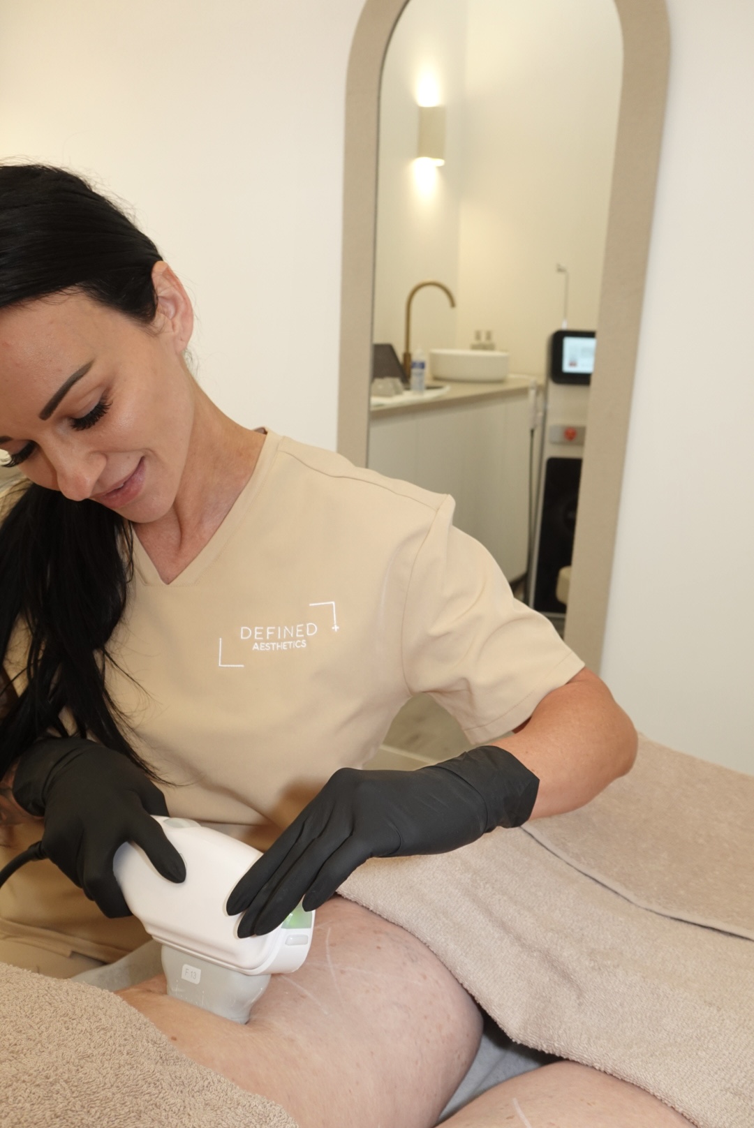 A practitioner using a treatment handpiece on a client’s upper thigh in the clinic