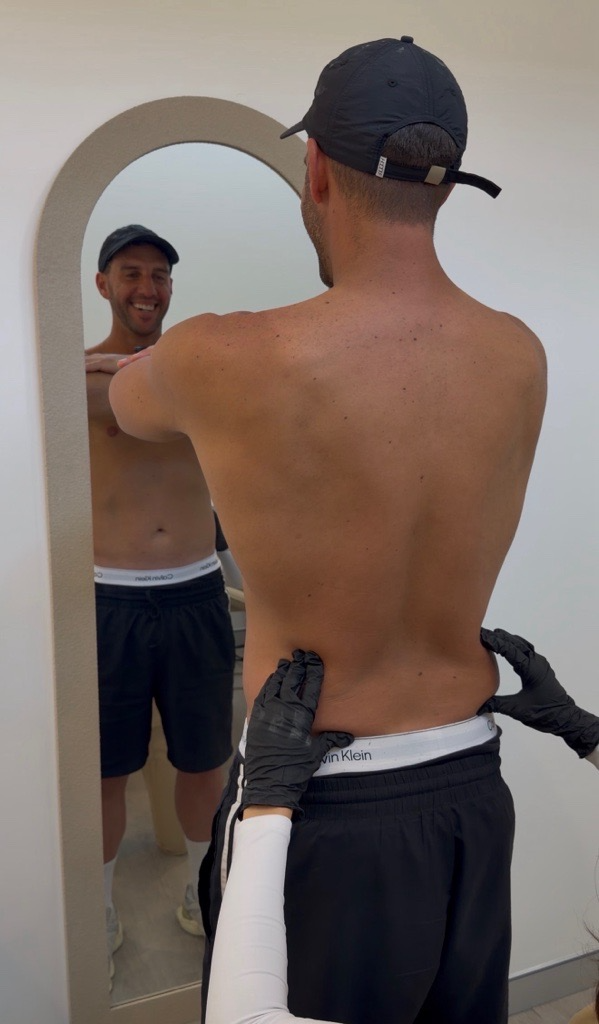 A man smiling into an arched mirror during a body consultation.