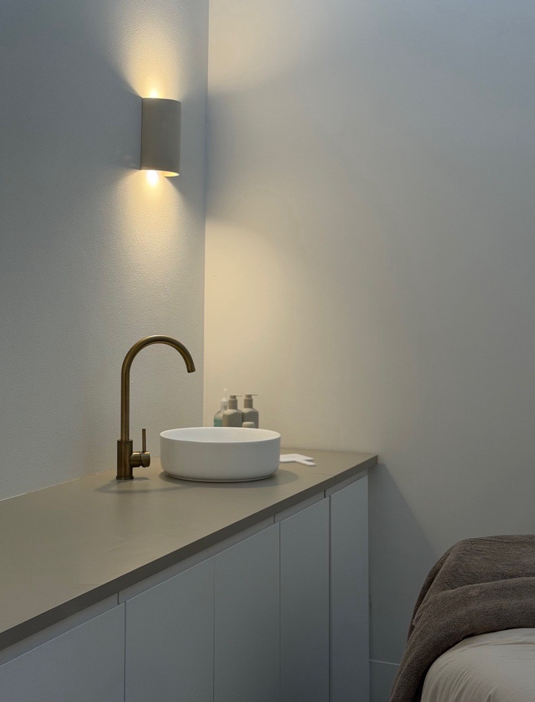 A calm treatment room with a basin, warm lighting and a treatment bed.