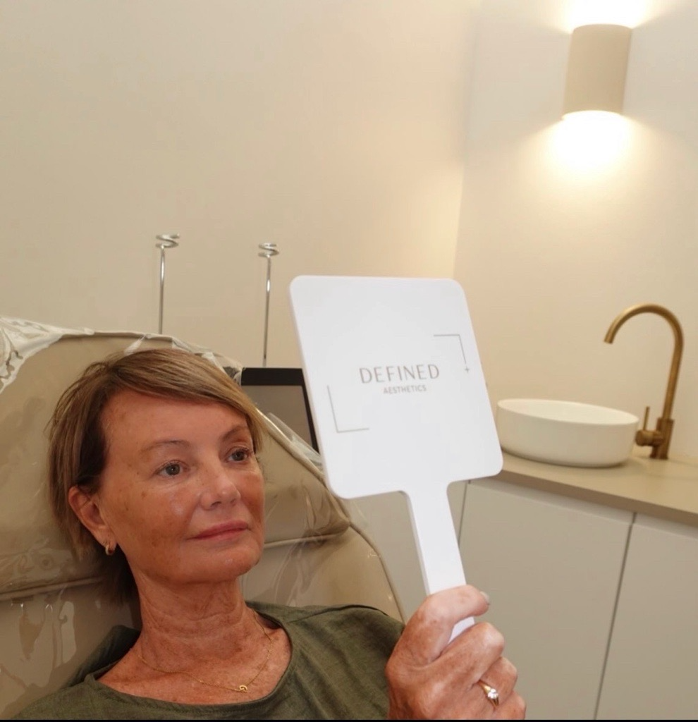 A client looking into a Defined Aesthetics hand mirror in the treatment room