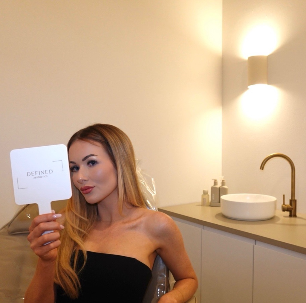 A client holding a Defined Aesthetics mirror in the treatment room.